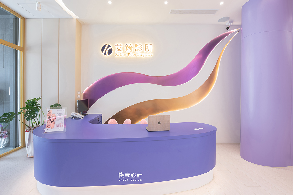 柒享設計作品高雄三民紫蘊之境醫療空間設計-艾錡診所接待區以柔和曲線與品牌識別牆相互呼應，運用紫色主體、流動線條及間接燈光勾勒空間層次，展現醫療專業與現代美學兼具的設計意象，帶來溫暖且安心的第一印象。